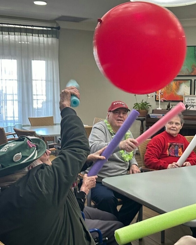 Seniors enthusiastically bat a large red balloon during a lively group activity at this senior living community near Hamilton Mill, GA, enjoying energetic and engaging programming.