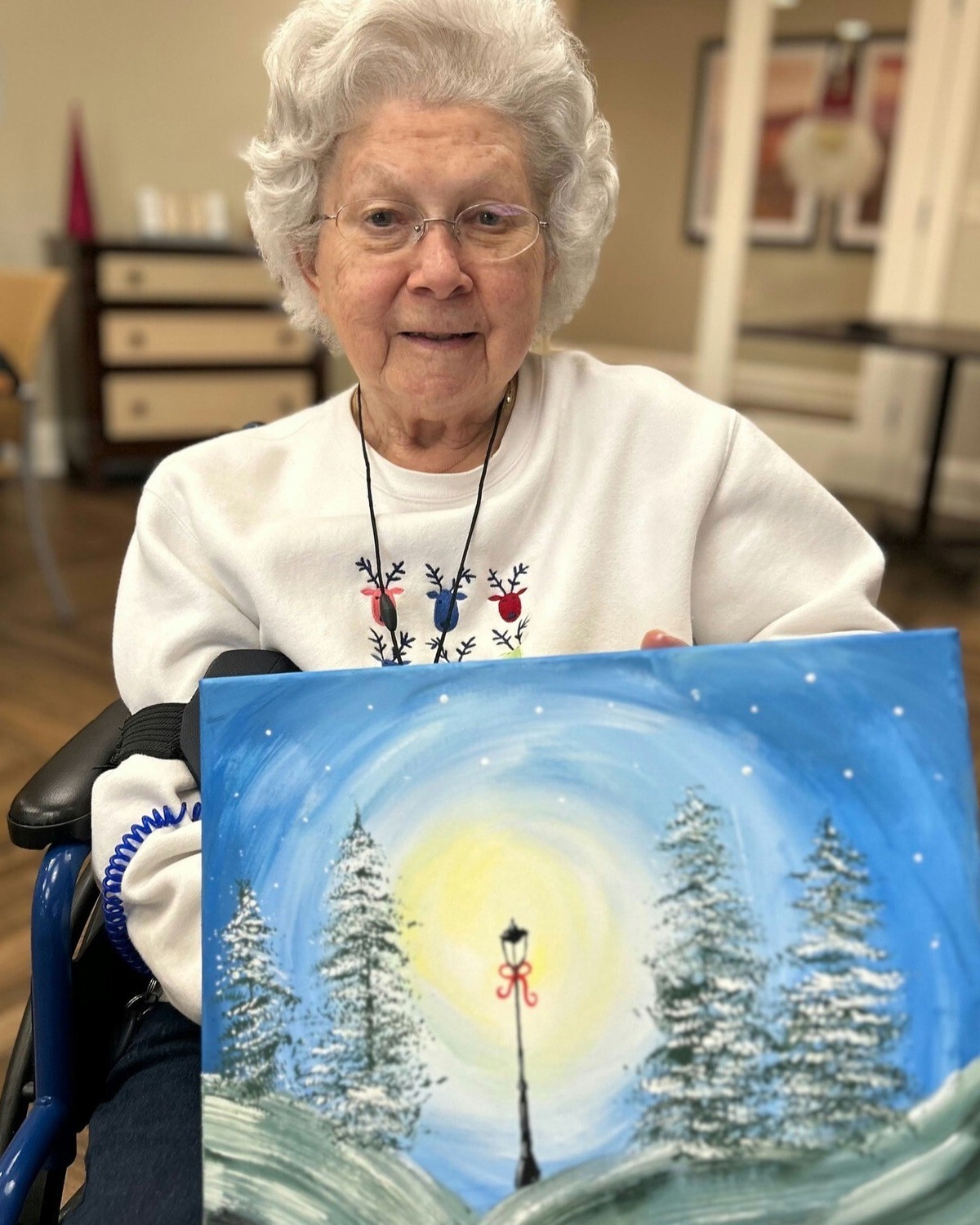 A senior proudly displays a beautiful winter landscape painting she created at this senior living community near Hamilton Mill, GA, showcasing the creative arts programming offered.