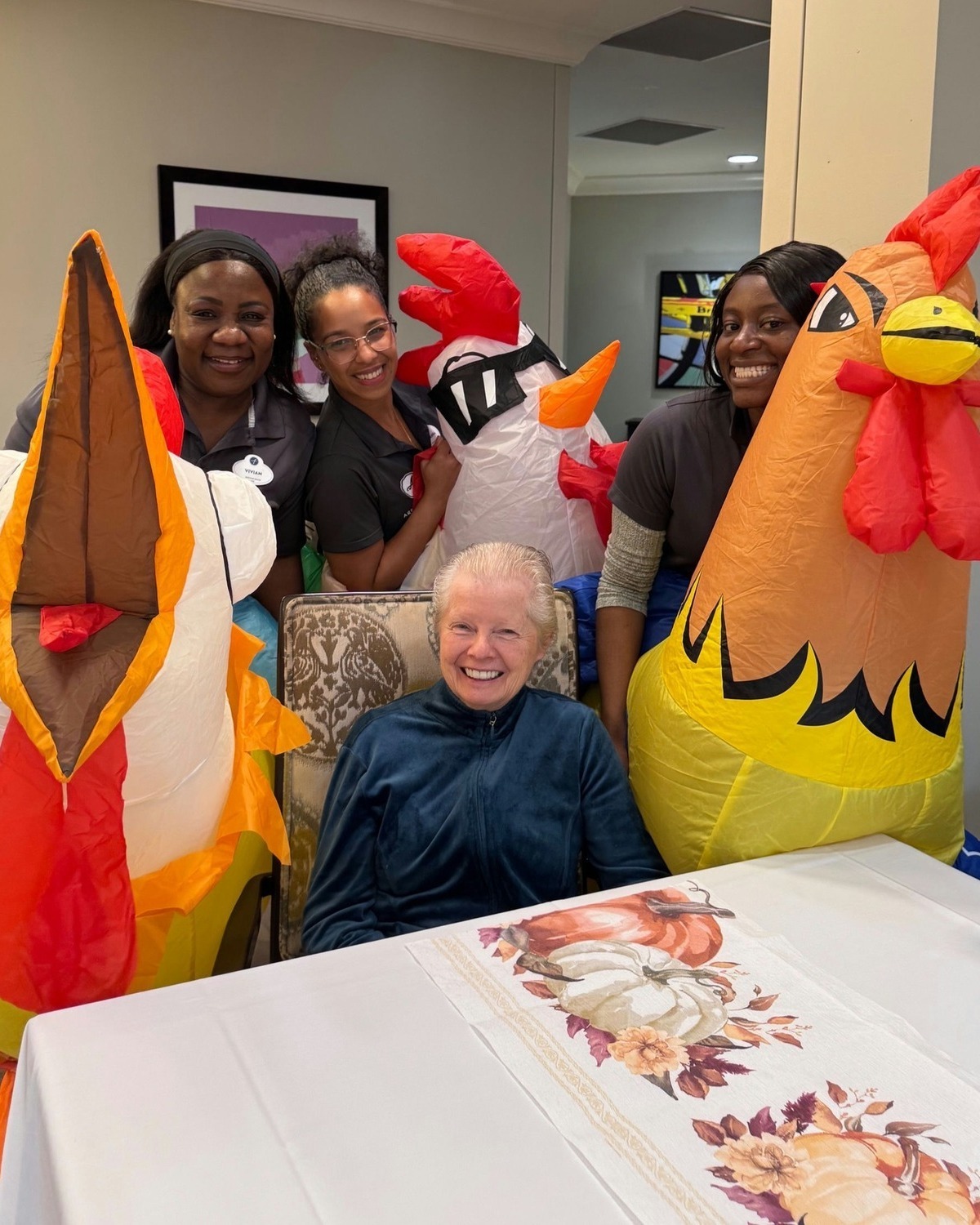 A senior resident smiles joyfully alongside staff in festive costumes during a fun community celebration, highlighting the engaging programs at this memory care Dacula Georgia community.
