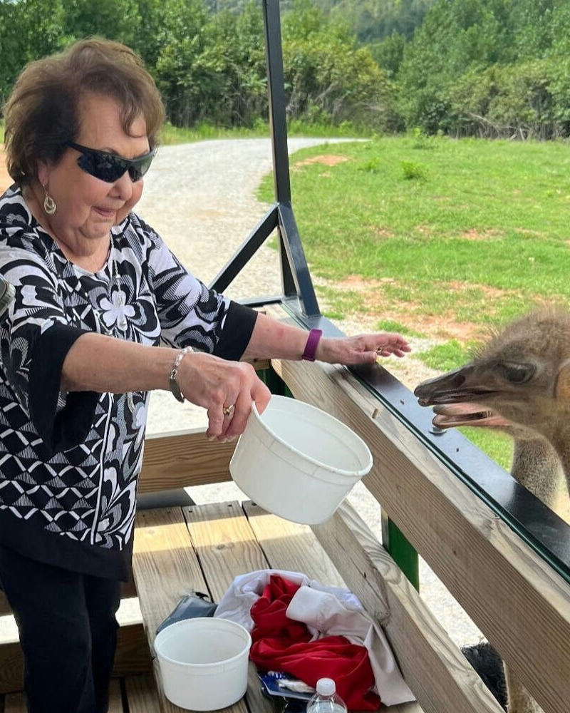 A senior resident enjoys a hands-on outdoor outing, feeding an animal at a local farm, reflecting the active senior lifestyle Dacula residents enjoy every day.