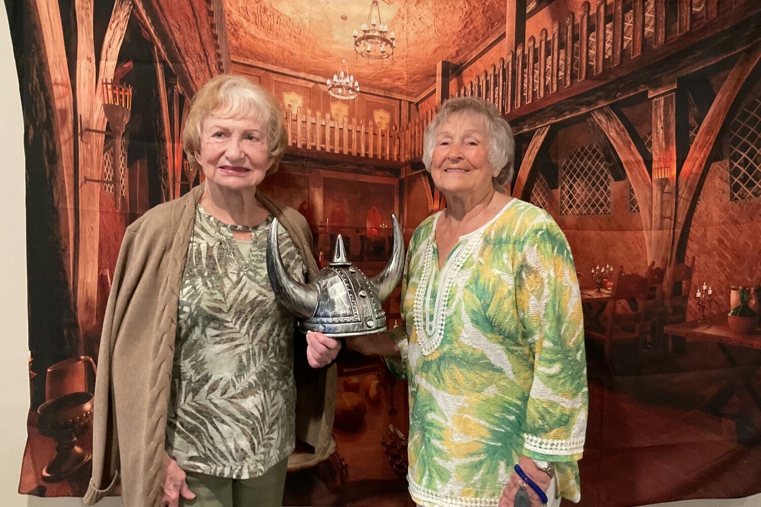 Two senior women posing together inside an ornate, warmly lit venue, one holding a trophy — a joyful moment reflecting the social and engagement-focused senior living Gwinnett County families love.