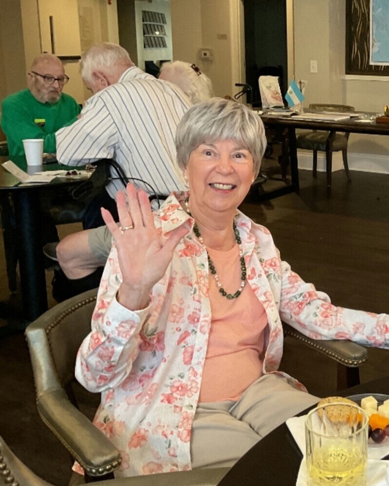 A senior resident waves cheerfully during a meal, enjoying the warm social atmosphere and senior living with gourmet dining Dacula GA has to offer.
