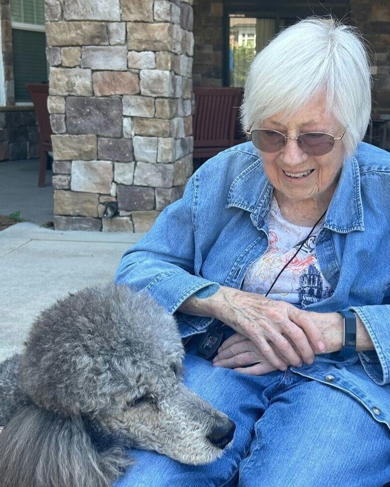 A senior resident enjoys a cheerful moment outdoors with a fluffy dog, reflecting the warm, pet-friendly senior living experience in Dacula GA.