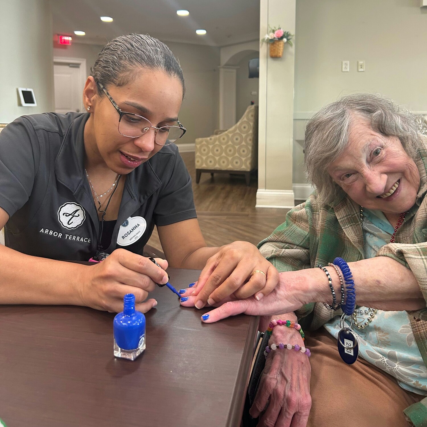 An Arbor Terrace staff member carefully painting a smiling resident's nails blue inside the community — reflecting the personalized senior care Dacula families trust for warm, everyday moments.