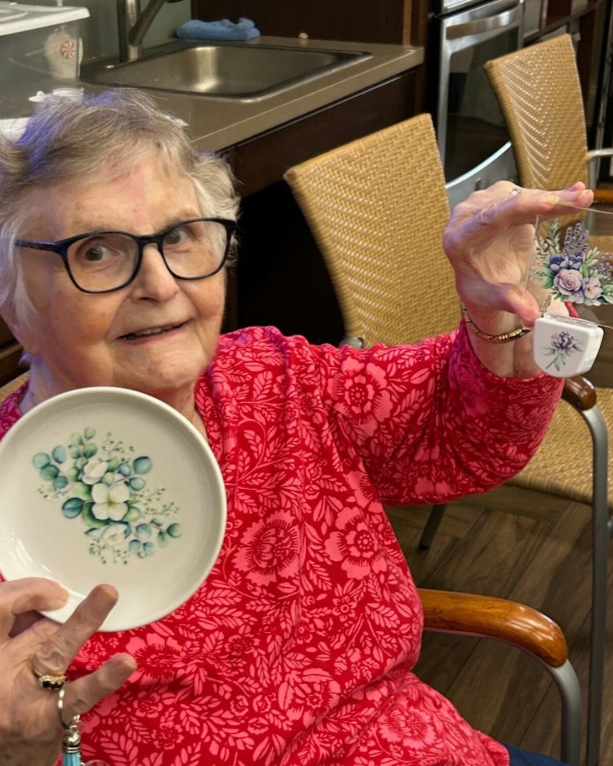 A senior resident smiles brightly while holding a decorative plate, enjoying hobbies and personal interests as part of daily life at this memory care Dacula Georgia community.