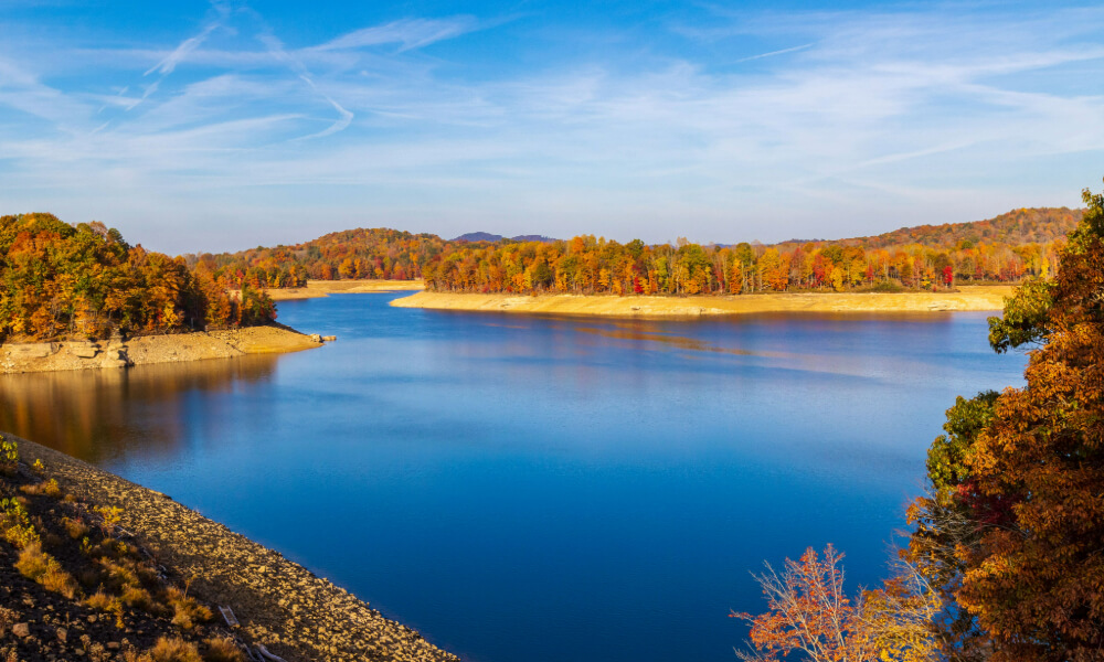 A serene lake surrounded by autumn-colored trees under a bright blue sky — the beautiful natural scenery near independent living Dacula GA, just a short drive from Lake Lanier.