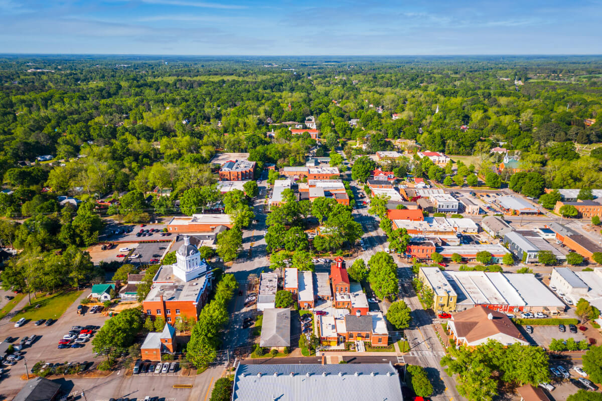 An aerial view of a charming, tree-lined town with small businesses and neighborhoods stretching into the distance — the welcoming community surrounding senior living Dacula Georgia at Arbor Terrace Hamilton Mill.