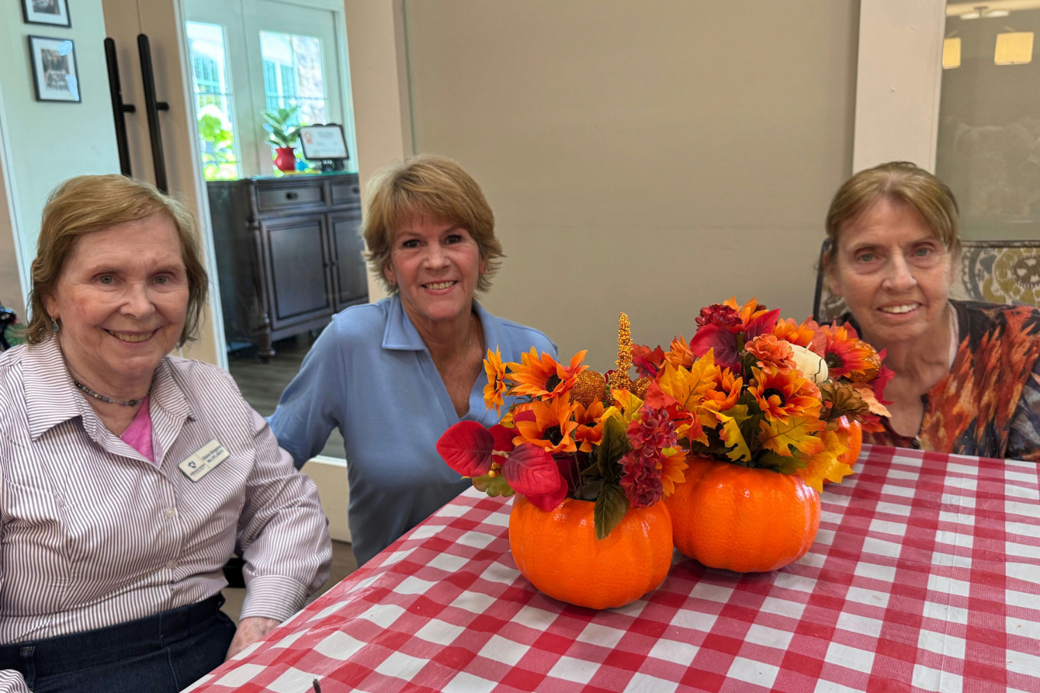 3 ladies smiling with fall themed flower arrangments