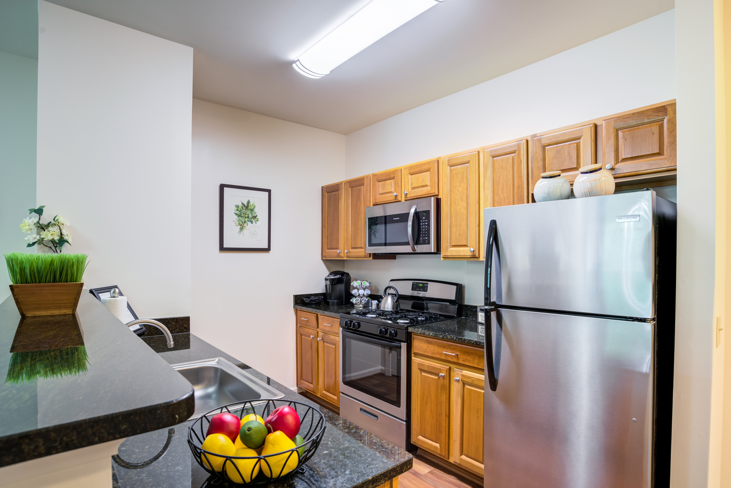 A fully equipped apartment kitchen at Arbor Terrace Herndon featuring stainless steel appliances, wood cabinetry, and hardwood floors, ideal for maintenance-free senior living in Herndon, VA.