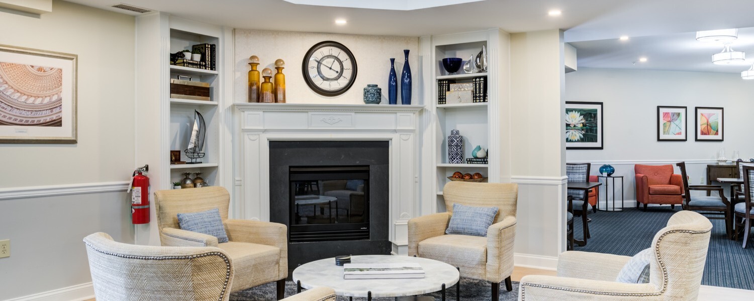 A warm and inviting common area lounge at Arbor Terrace Herndon featuring a classic fireplace, comfortable seating, and elegant decor, perfect for independent senior living in Herndon, VA.