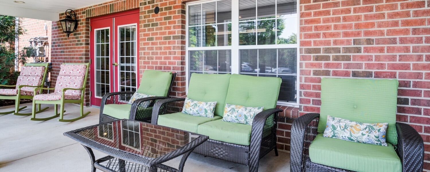 A charming outdoor patio at Arbor Terrace Herndon featuring green cushioned seating and brick surroundings, offering a relaxing retreat for seniors in the Herndon, VA community.