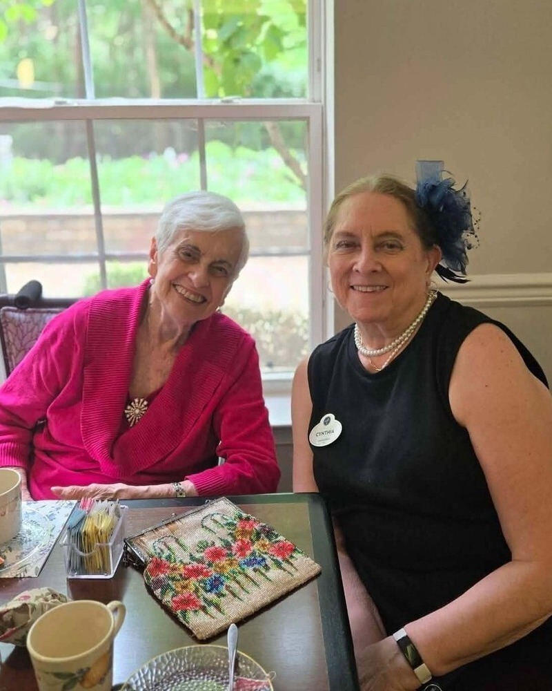 A resident and staff member share warm smiles at an elegant tea table by a sunlit window, reflecting a treasured senior living with dining and activities Herndon moment at Arbor Terrace Herndon, a welcoming senior living Herndon Virginia community.