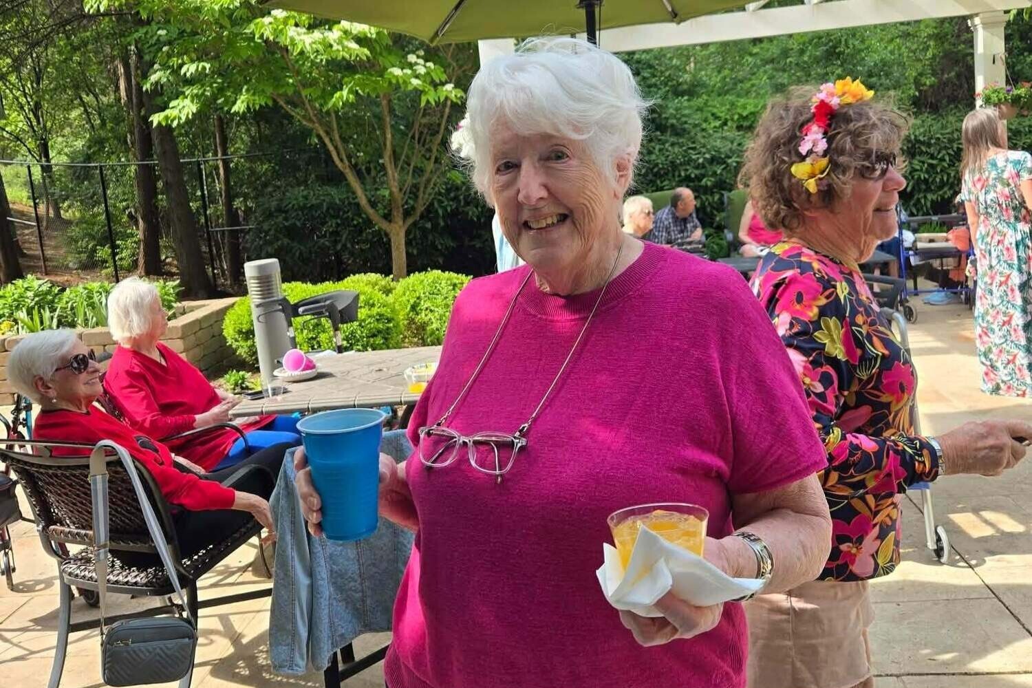 A resident smiles warmly while holding a treat during an outdoor garden gathering surrounded by friends, reflecting the vibrant senior living with dining and activities Herndon at Arbor Terrace Herndon, a lively senior living Herndon Virginia community.