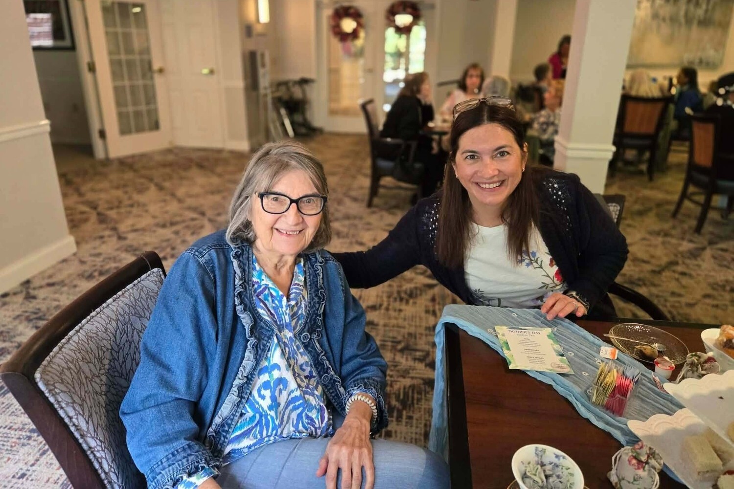 A resident shares a warm smile with a visitor at an elegantly set dining table, reflecting the welcoming senior living with dining and activities Herndon at Arbor Terrace Herndon, a senior living Herndon Virginia community.