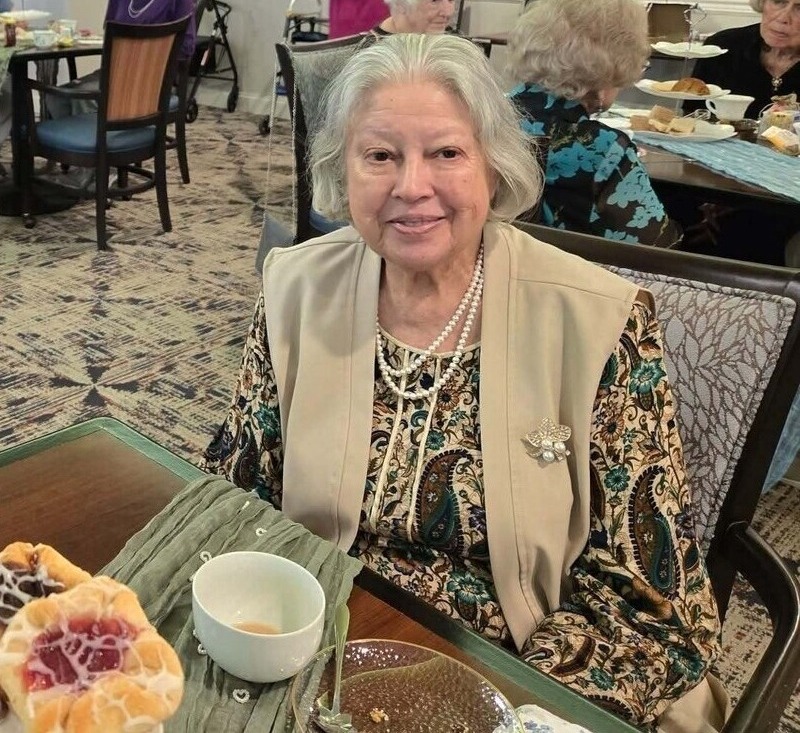 A resident smiles warmly at an elegant dining table set with tea, showcasing the delightful senior living with dining and activities Herndon offers at Arbor Terrace Herndon, a welcoming senior living Herndon Virginia community.