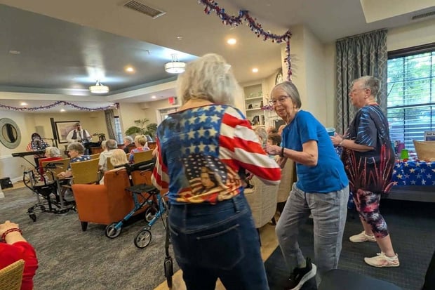 Residents dance and mingle together at a festive patriotic gathering decorated with red, white, and blue streamers, reflecting the lively senior living with dining and activities Herndon at Arbor Terrace Herndon, a vibrant senior living Herndon Virginia community.