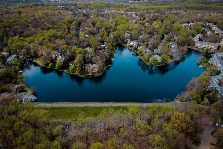 An aerial view of Reston's sparkling lake and wooded shoreline captures the vibrant town center lifestyle just minutes from Arbor Terrace Herndon, offering convenient independent living Reston VA access near this senior living Herndon Virginia community.