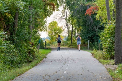 Two walkers enjoy the shaded, paved path of the W&OD Trail, reflecting the active senior lifestyle near W&OD Trail that residents cherish at Arbor Terrace Herndon, a vibrant senior living Herndon Virginia community.
