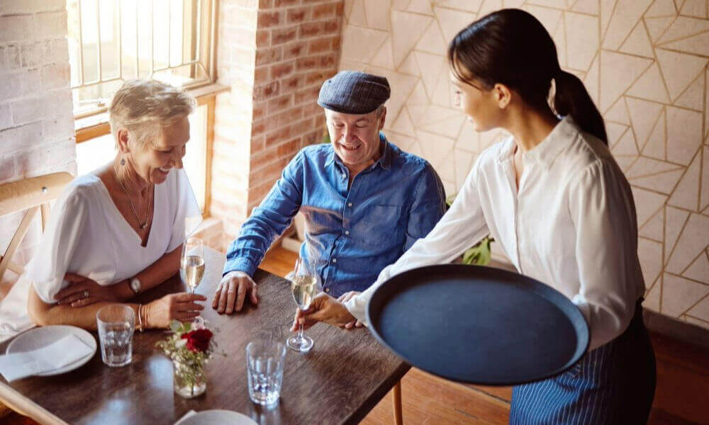 Two older adults and a younger companion share a meal together at a warm, inviting local restaurant, reflecting the vibrant dining scene near senior living in Herndon, Virginia.
