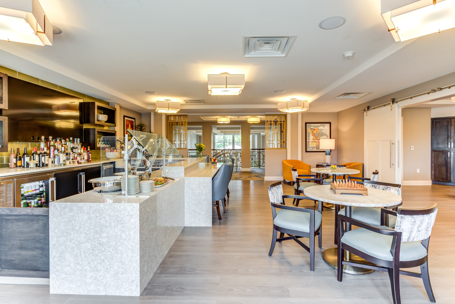 Bright community lounge with a stone-top bar, cozy dining tables, and a chess set, part of the amenities at our senior living community in Highland Park, IL, made for an active senior lifestyle.