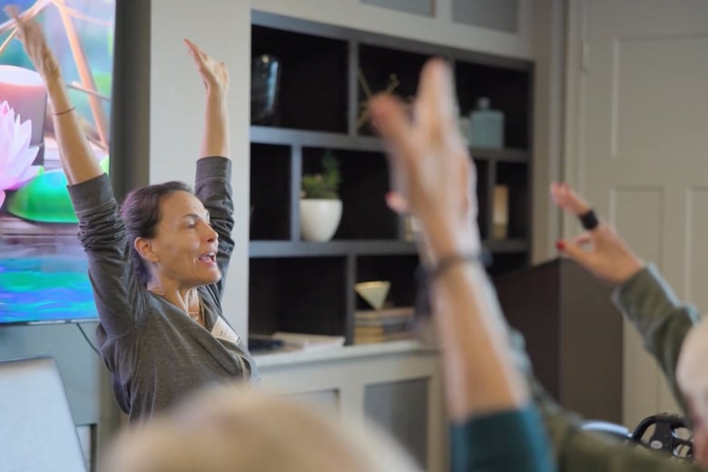 An instructor leads residents through an energizing stretch class in a bright activity room, reflecting the active, engaging senior living lifestyle offered throughout this senior living community.