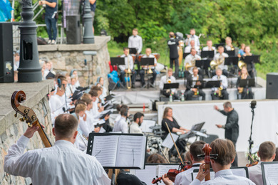 Musicians dressed in white play cellos and brass instruments on a leafy outdoor stage as a conductor leads the performance, a memorable outing for a senior community near Ravinia Festival grounds and a vibrant part of senior living Highland Park IL.