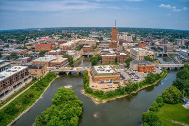 Aerial view of a charming downtown with brick buildings, tree-lined streets, and a winding river framed by lush parkland, a lively setting close to senior apartments near downtown Highland Park that supports an active senior lifestyle Highland Park IL.