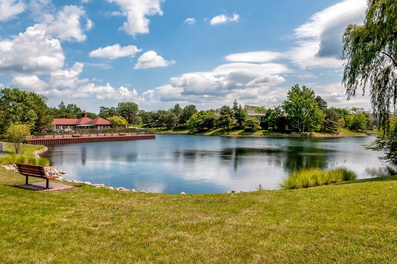 A calm pond reflects puffy white clouds and leafy trees along a grassy shoreline, a peaceful outdoor scene for families considering senior living near Northbrook IL and nature-friendly senior living Highland Park IL.