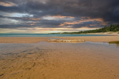 Golden sand meets shallow, rippling water along a quiet shoreline beneath a dramatic sunset sky, a peaceful lakeside view for senior living near Lake Michigan Highland Park and a calming escape for wellness-focused senior living North Shore.