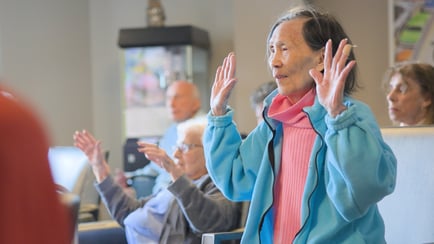 Residents raise their hands together during a lively wellness class at Arbor Terrace Highland Park, reflecting the active senior lifestyle in Highland Park, IL. Wellness-focused senior living brings people together on Chicago's North Shore.