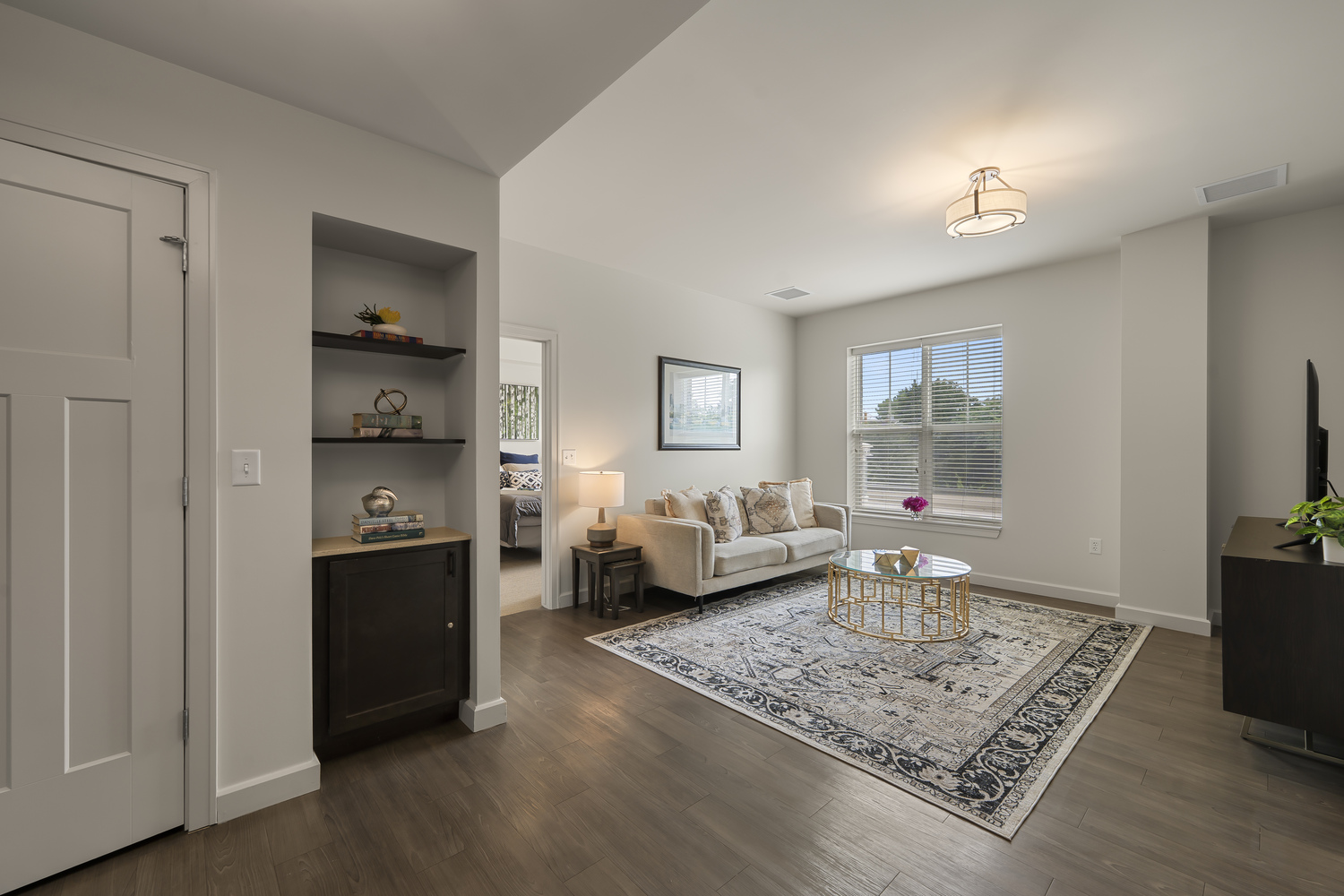 A cozy living room features a cream sofa, patterned area rug, and gold coffee table, with built-in shelving and a glimpse of the bedroom beyond, showcasing an apartment at our senior living Highland Park IL community and its active senior lifestyle Highland Park IL.