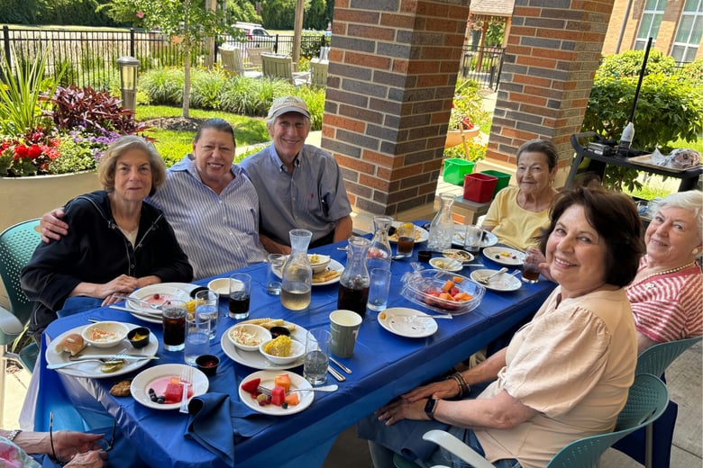 Senior residents and family members sitting around a table filled with food and smiling