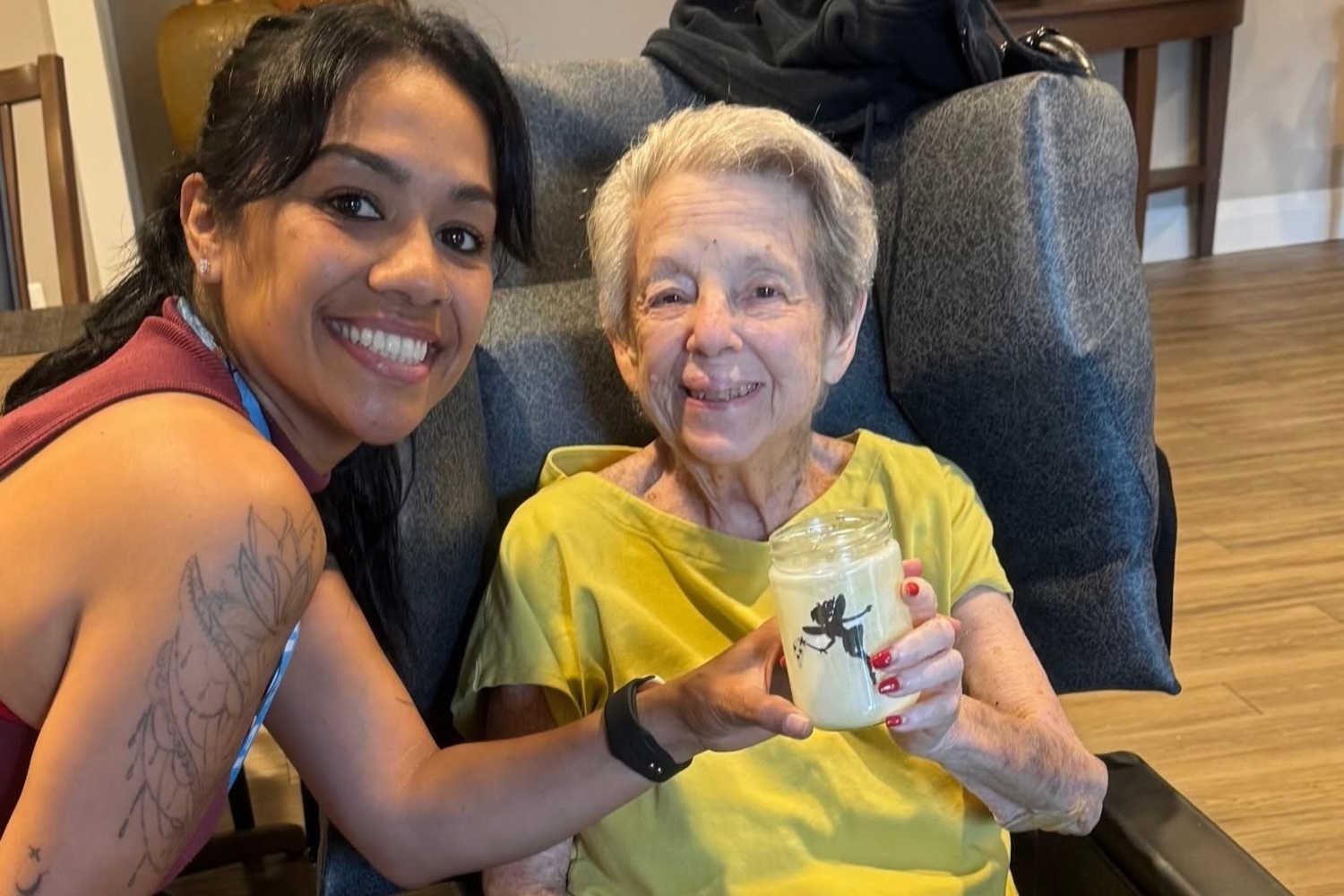 A smiling woman leans in close to a community member in a yellow top who proudly holds up a decorated jar, sharing a warm moment at Arbor Terrace Highland Park that reflects personalized senior care Highland Park IL and welcoming senior living Highland Park IL.