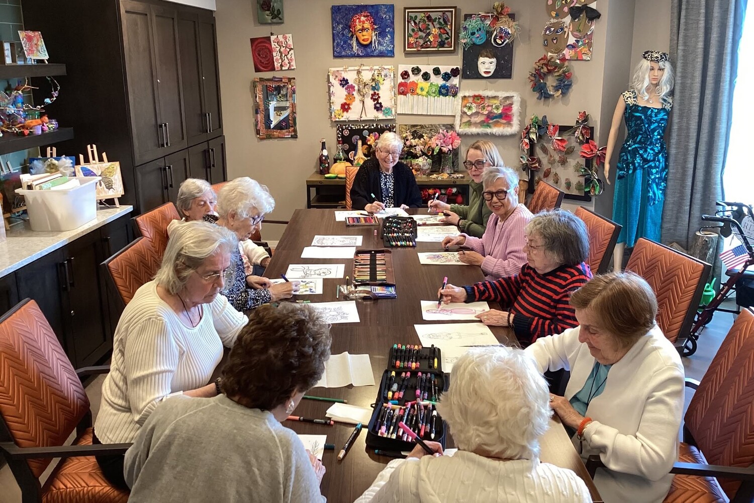 Community members draw and color around a long table surrounded by colorful artwork, masks, and a dress form at Arbor Terrace Highland Park, one of the top senior living communities Lake County IL, where creativity is part of an active senior lifestyle Highland Park IL.