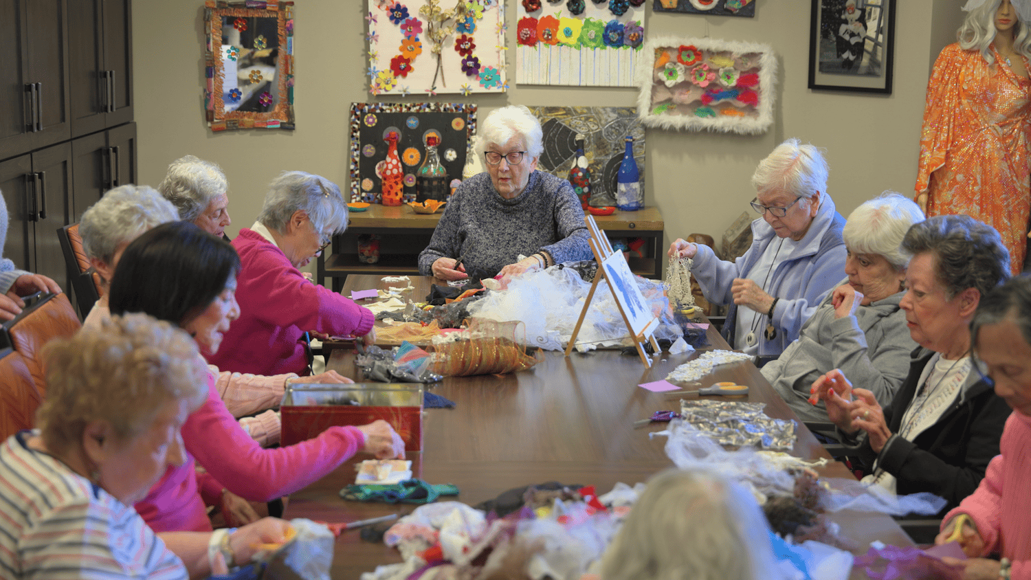 A large group of residents work on a textile craft project together, surrounded by colorful art, at our senior living community in Highland Park, IL.