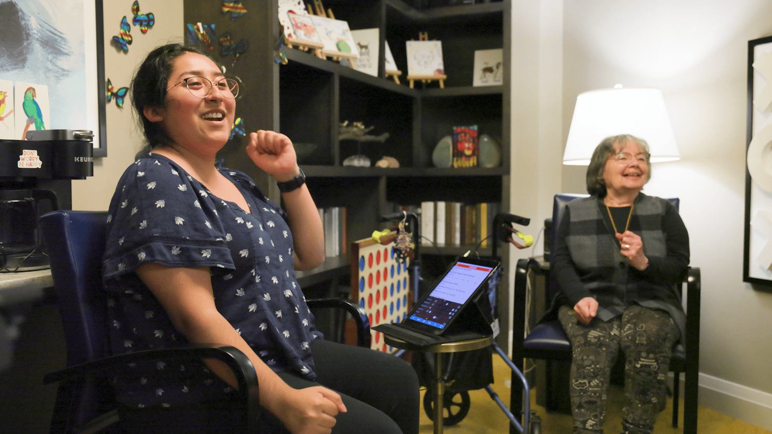 A staff member shares a laugh with a resident near a Connect Four game and art display at our senior living community in Highland Park, IL.
