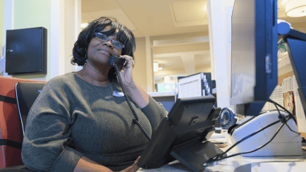 A smiling staff member answers a call at the front desk of Arbor Terrace Highland Park, ready to help with questions about senior living in Highland Park, IL. This kind of warm service reflects senior care Highland Park, Illinois, families trust.