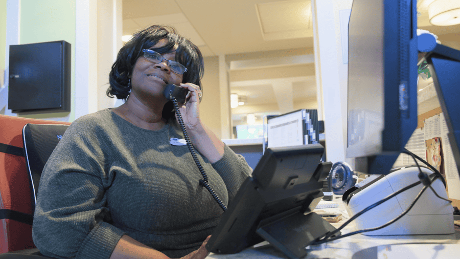 A smiling staff member answers a call at the front desk of Arbor Terrace Highland Park, ready to help with questions about senior living in Highland Park, IL. This kind of warm service reflects senior care Highland Park, Illinois, families trust.