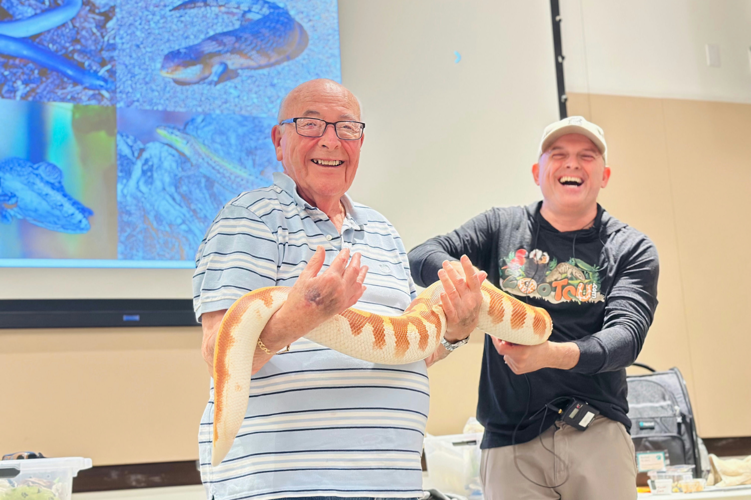 Senior man holding a snake being helped by handler