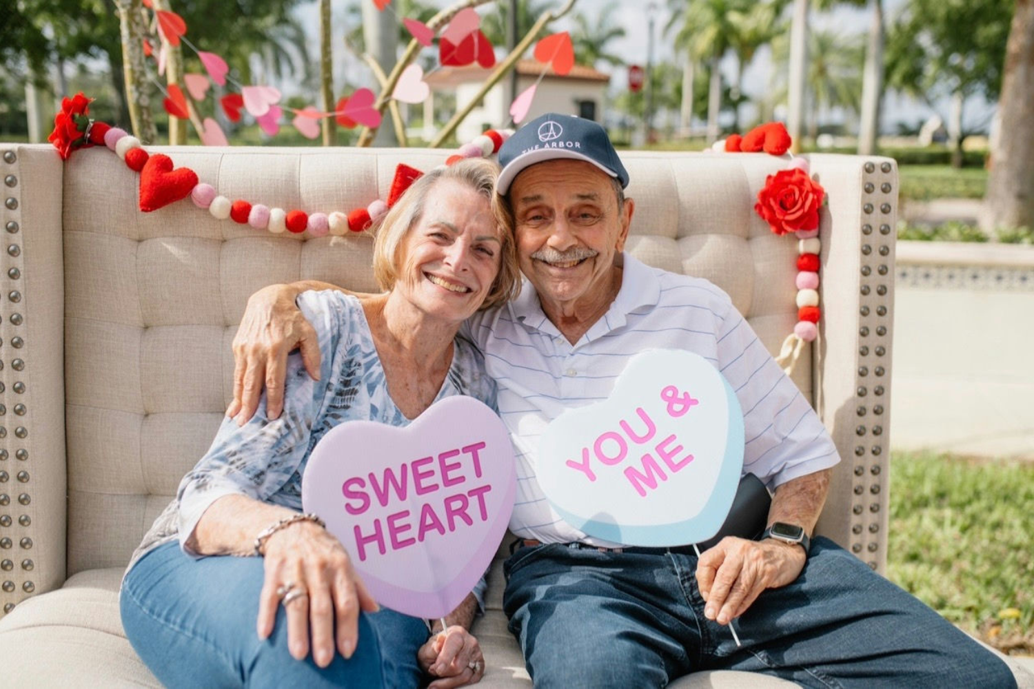 Senior man and woman sitting on a couch holding valentines day signs