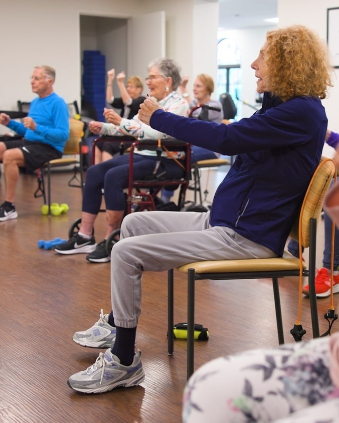 A group of residents participating in a seated exercise class using resistance bands at this wellness-focused senior living community in Lake Worth, FL, staying active together in a spacious fitness room.