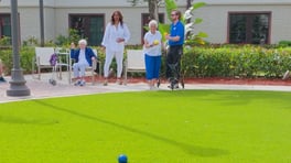 Residents gathered around the courtyard green playing bocce ball on a sunny day at The Arbor at Lake Worth