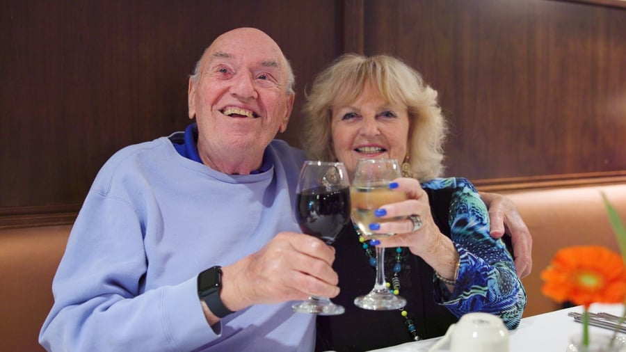 Residents couple in blue cheersing with glasses of red and white wine while sitting in the dining room  