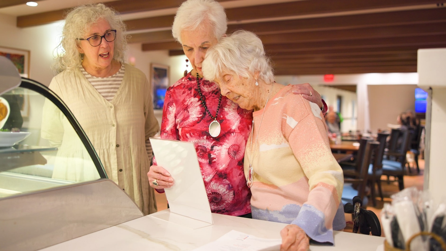 a group of senior ladies standing in front of the dining area bar counter at the Arbor at Lake Worth, holding a menu