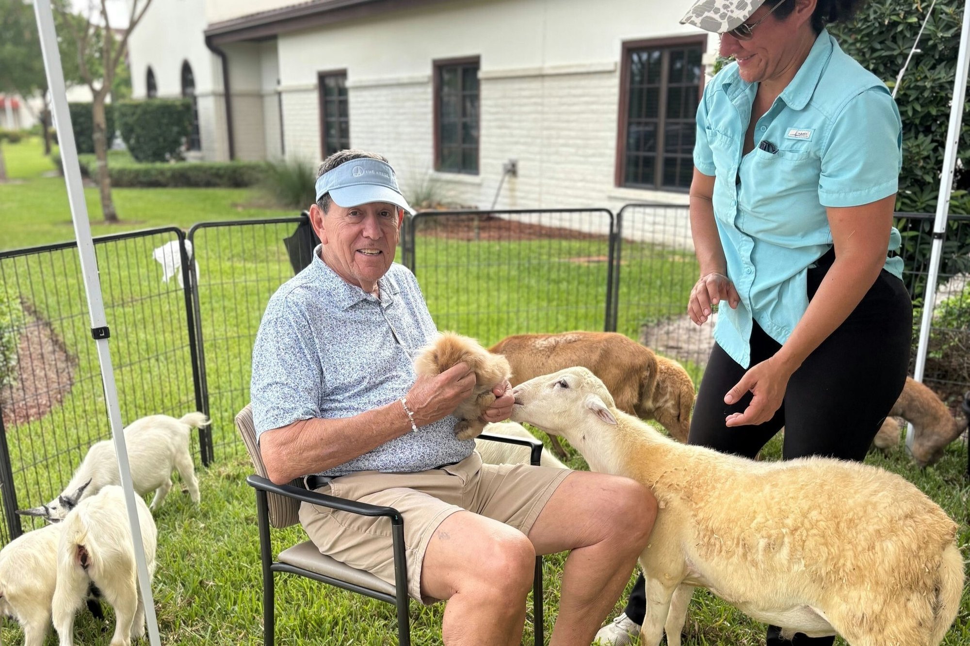a senior man sitting on a chair while holding a bunny from a a petting zoo with goats and rabbits while a staff member stands close by