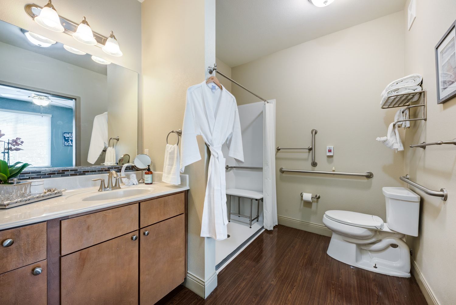 Clean, well-appointed bathroom at Arbor Terrace Lakeway TX, featuring wood-toned cabinetry, a grab bar for added safety, a hanging robe, and thoughtful details suited for assisted living residents.