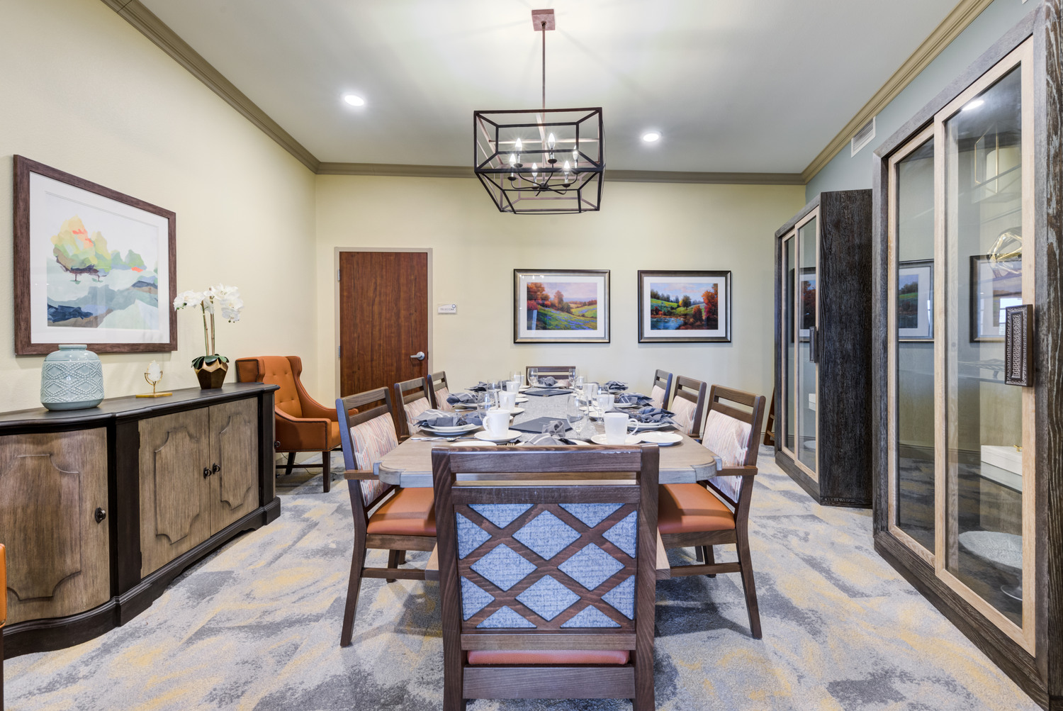 Elegant private dining room at Arbor Terrace Lakeway TX assisted living, featuring a decorative chandelier, upholstered dining chairs, landscape artwork, and a warm ambiance perfect for special family gatherings.
