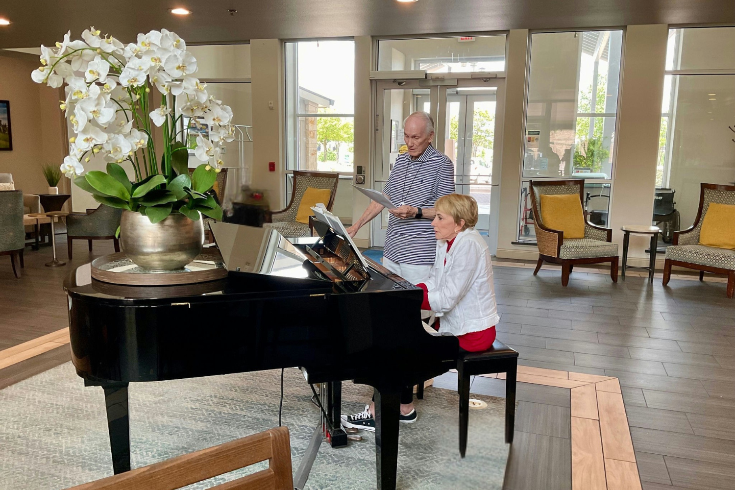 A resident plays a grand piano in a sunlit, elegantly furnished common area at this senior living community in Lakeway, TX, sharing the gift of live music with fellow residents at Arbor Terrace.