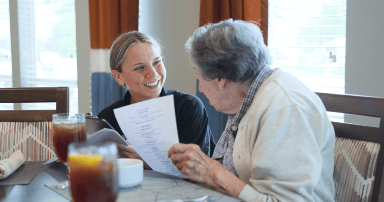 Resident and staff member sitting at a table with drinking discussing information on a sheet of paper 