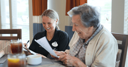 A smiling staff member sits with an older adult at a dining table, reviewing paperwork together at Arbor Terrace Lakeway — warm, personalized senior care in Lakeway, TX.